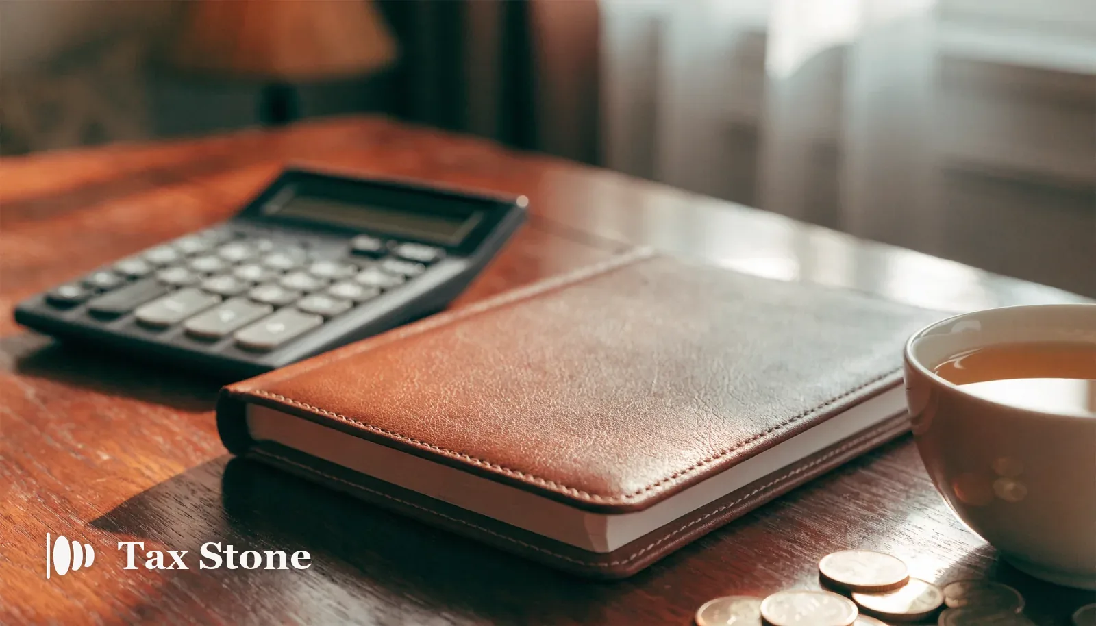 A leather accounts ledger, calculator and cup of tea beside British pound coins — TaxStone UK self-employed Self Assessment tax calculator
